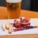 A pint of beer next to some ham and bread sticks